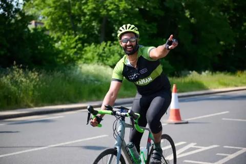Anthony Nolan supporter smiling and waving on his bike at RideLondon 2023