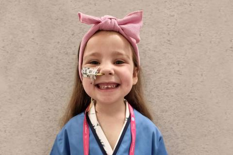 a little girl wearing a nurses uniform with a bow in her hair and an NG tube