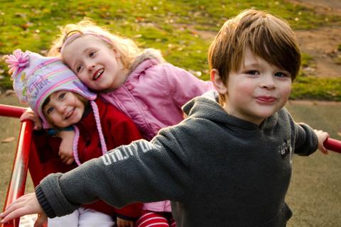 Ben and his two sisters smiling at the camera in the playground