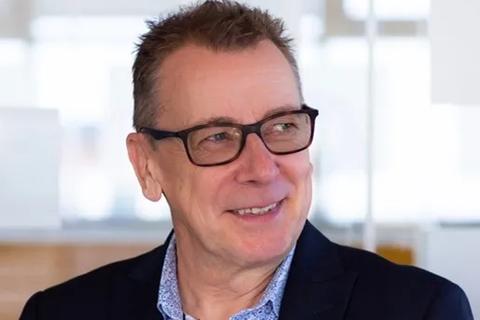 A white middle aged male in glasses. He is wearing a blue patterned shirt and navy suit jacket