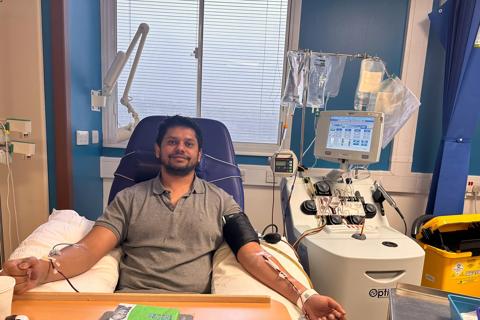 a young Indian man in a hospital bed, with wires connected to his arms, he's wearing a grey t-shirt and smiling