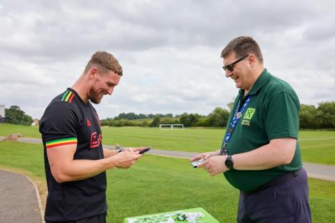 A football player signing up to the Anthony Nolan register on his mobile phone, with an Anthony Nolan volunteer