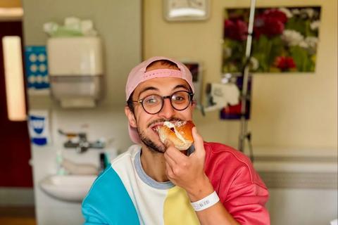 A photo of Dan sitting on a hospital bed, eating a doughnut.