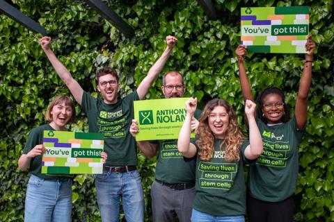 A group of men and women wearing Anthony Nolan tshirts cheering and holding branded signs