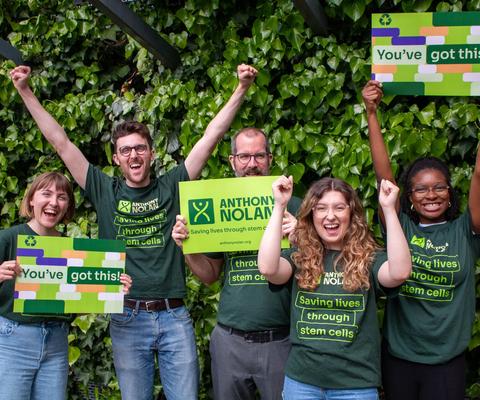 A group of men and women wearing Anthony Nolan tshirts cheering and holding branded signs