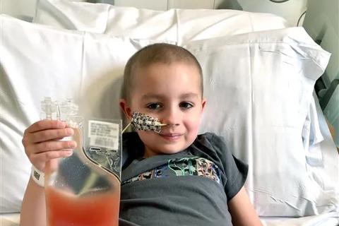 A little boy lying in a hospital bed holding up a bag of lifesaving stem cells