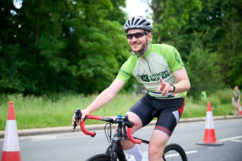 A man cycling on a bike in his Anthony Nolan RideLondon race shirt while doing a peace sign