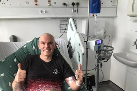 Ricky in a hospital bed smiling with his thumbs up to the camera