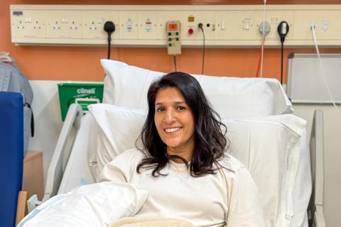 A female member of staff lying in a hospital bed donating stem cells smiling at the camera