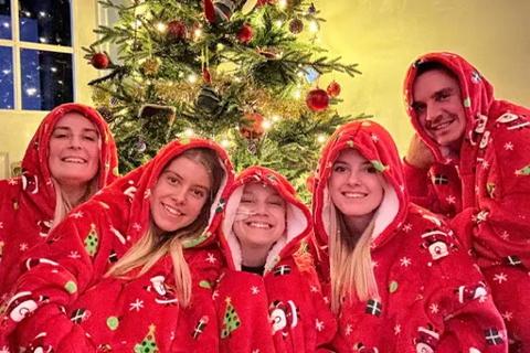 a family of five in matching red christmas onesies in front of a christmas tree