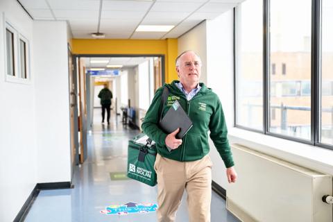 Volunteer courier walks through hospital corridor with courier bag.