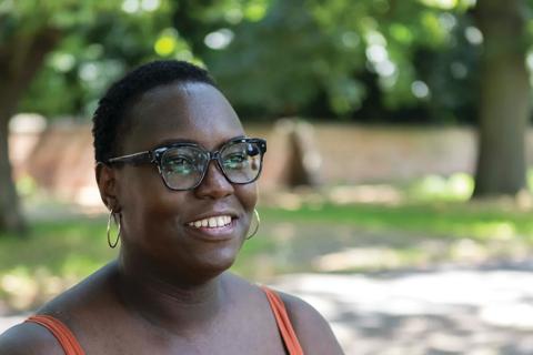 A black woman smiling and looking away from the camera sat outside on a sunny day