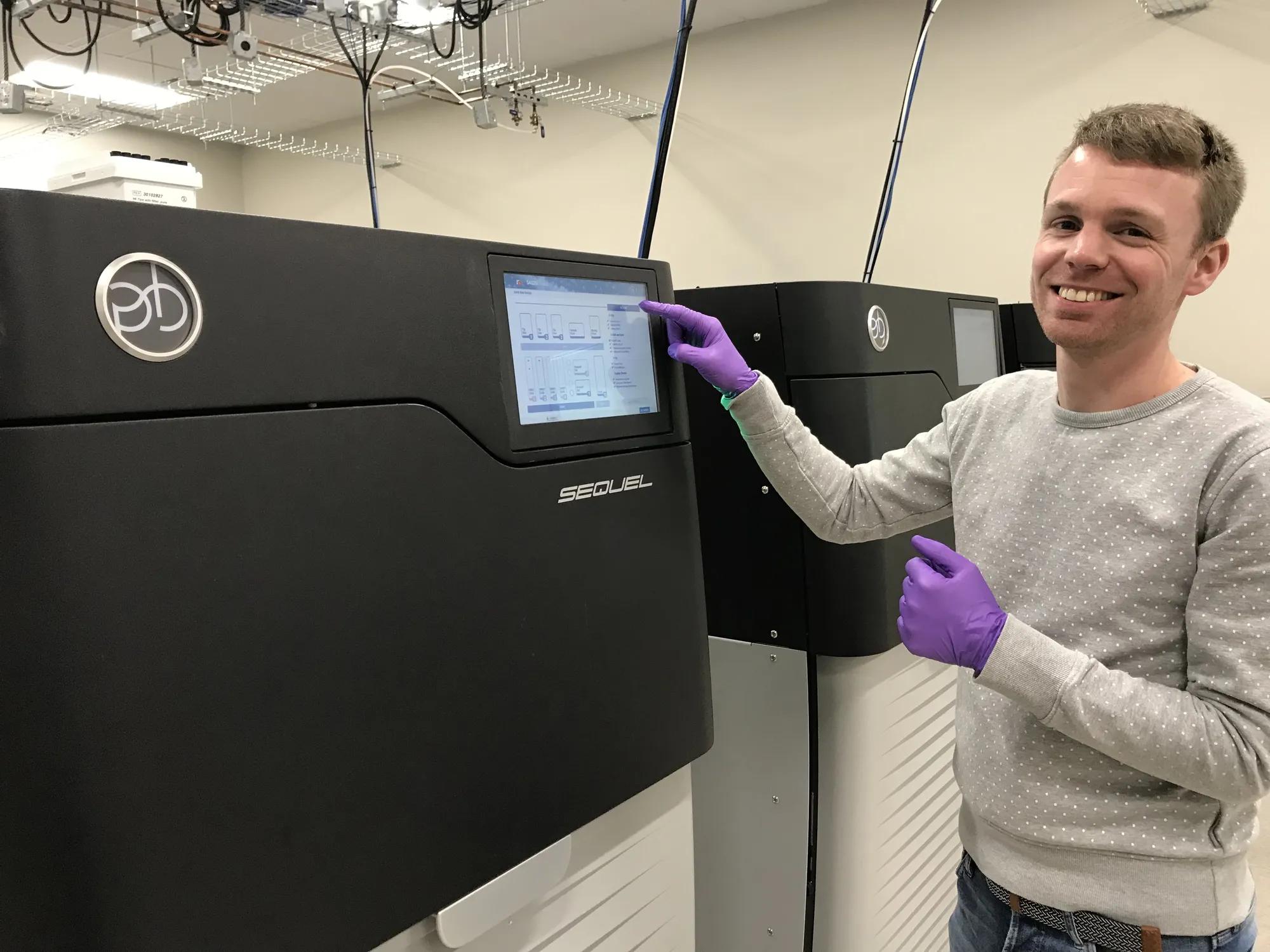 A smiling scientist standing next to a large boxy machine