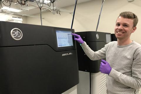 A smiling scientist standing next to a large boxy machine