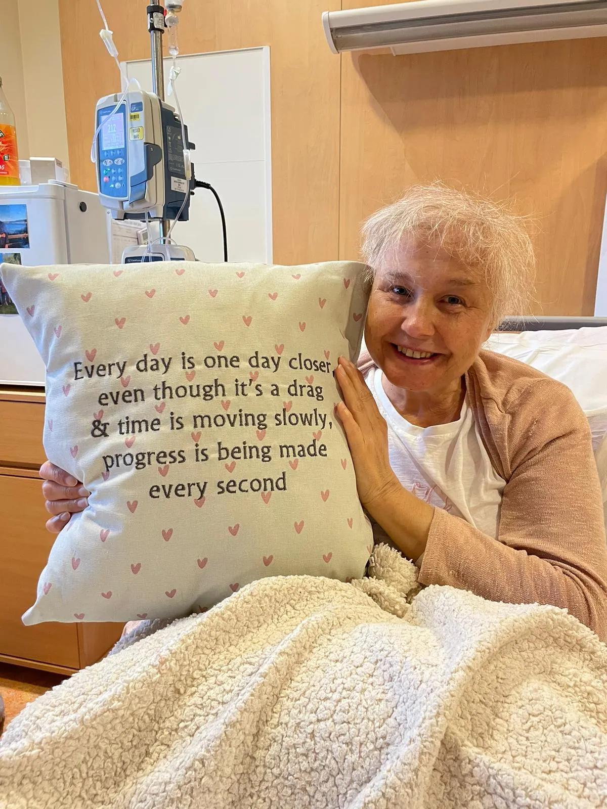 a woman in a hospital bed holding up a cushion with embroidered words