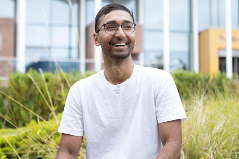 a young indian man laughing and looking off camera, he is wearing glasses and a white t-shirt