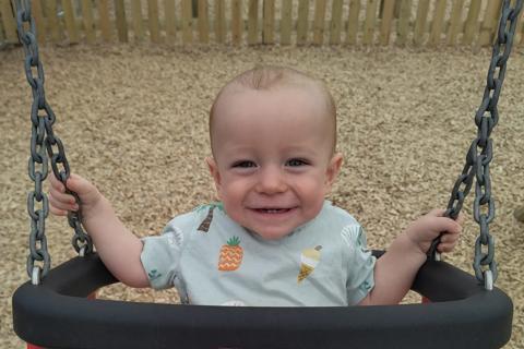 A baby boy sits in a red children's swing