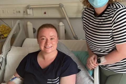 Emma, a young women with blonde curly hair, with her sister who is sitting in a hospital bed