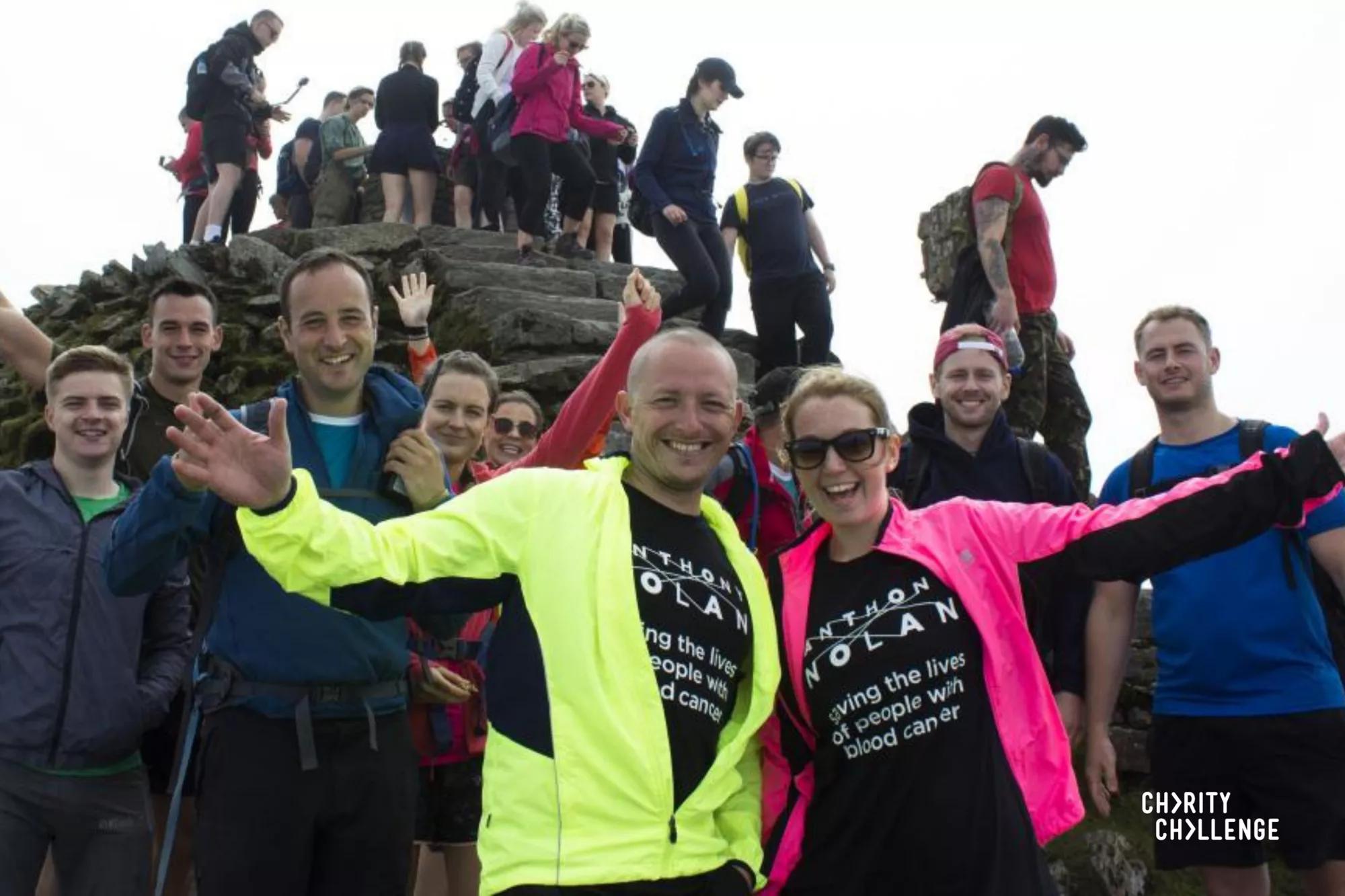 Photo of a group of people posing at the top of a peak. The people in the forefront are wearing Anthony Nolan t-shirts