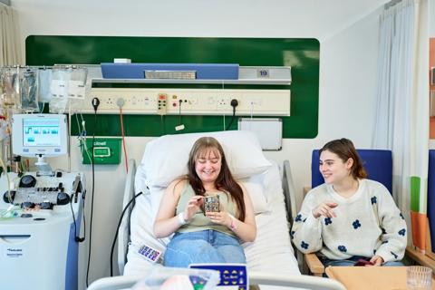 Donor sits on hospital bed smiling while talking to friend sitting next to her.