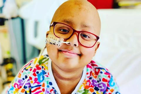 10-year-old Zara, a stem cell transplant recipient, in hospital, smiling wearing a colourful jumper.