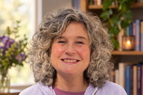 Michelle holding her book, she is wearing a lilac top and has shoulder length curly grey hair