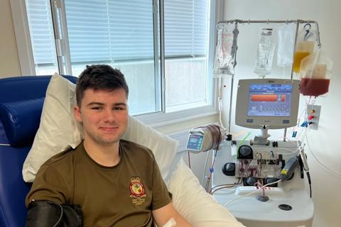 a young man in a hospital bed, he is wearing a grey t-shirt and he is smiling