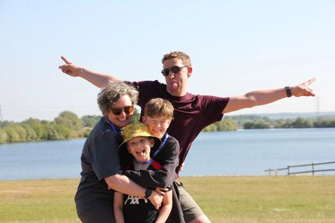 A mother hugs her two sons while the dad stands behind them posing with his arms outstretched and his tongue stuck out