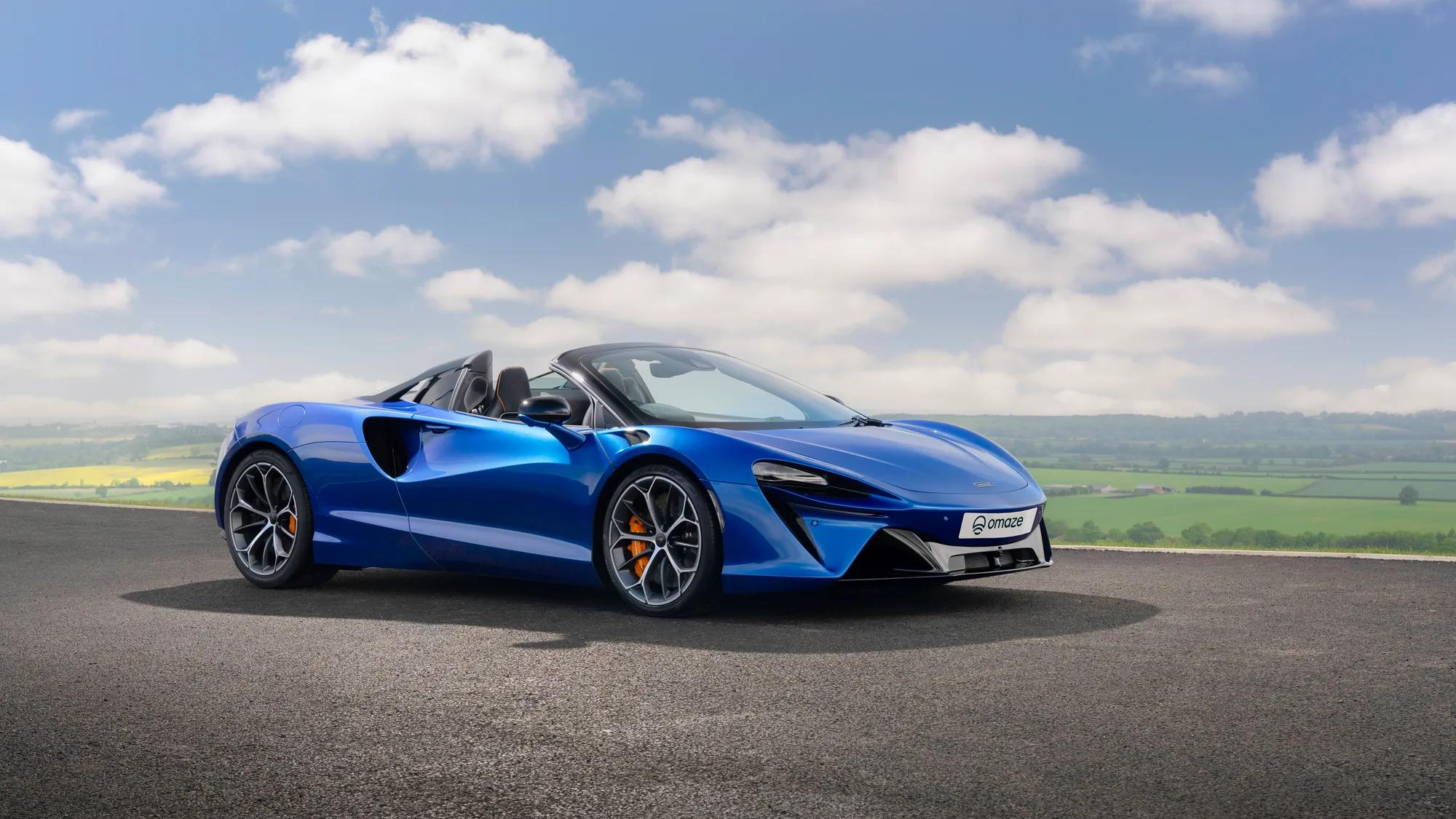 A dark blue McLaren Artura Spider sports car with the English countryside in the background