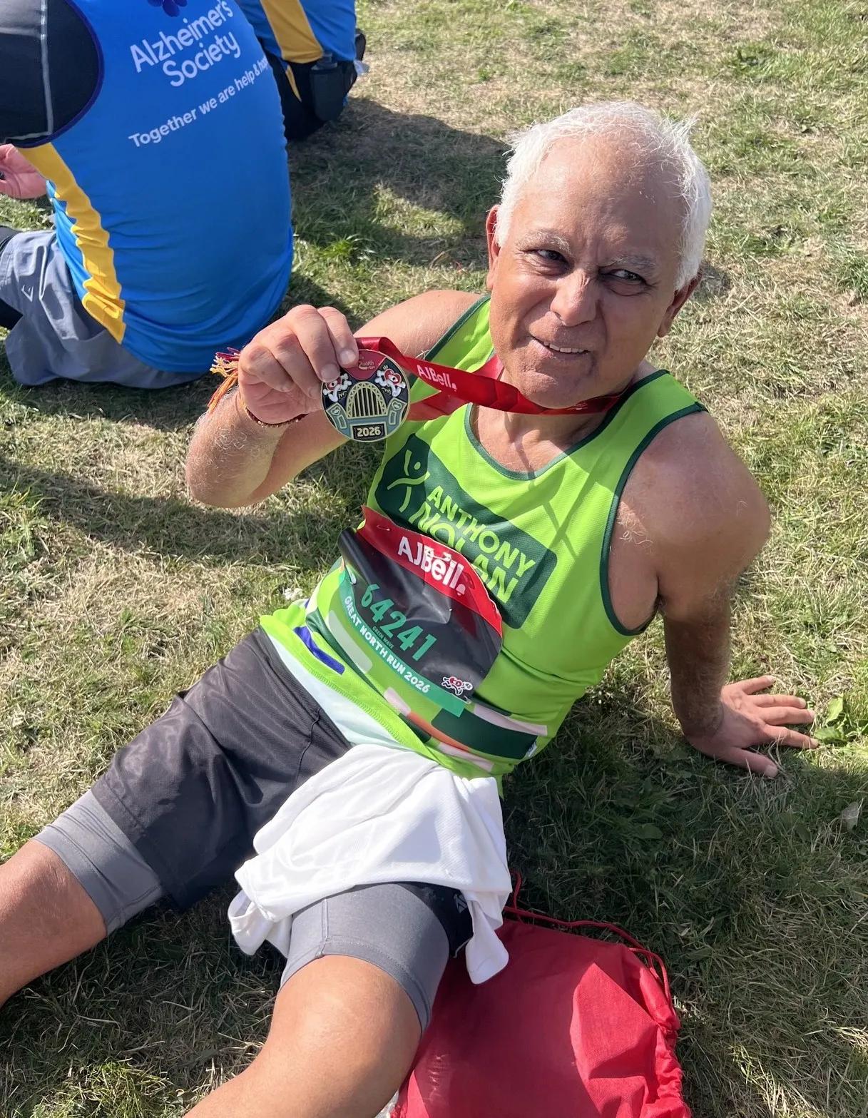 a man sitting on the grass in his AN running vest holding his race medal