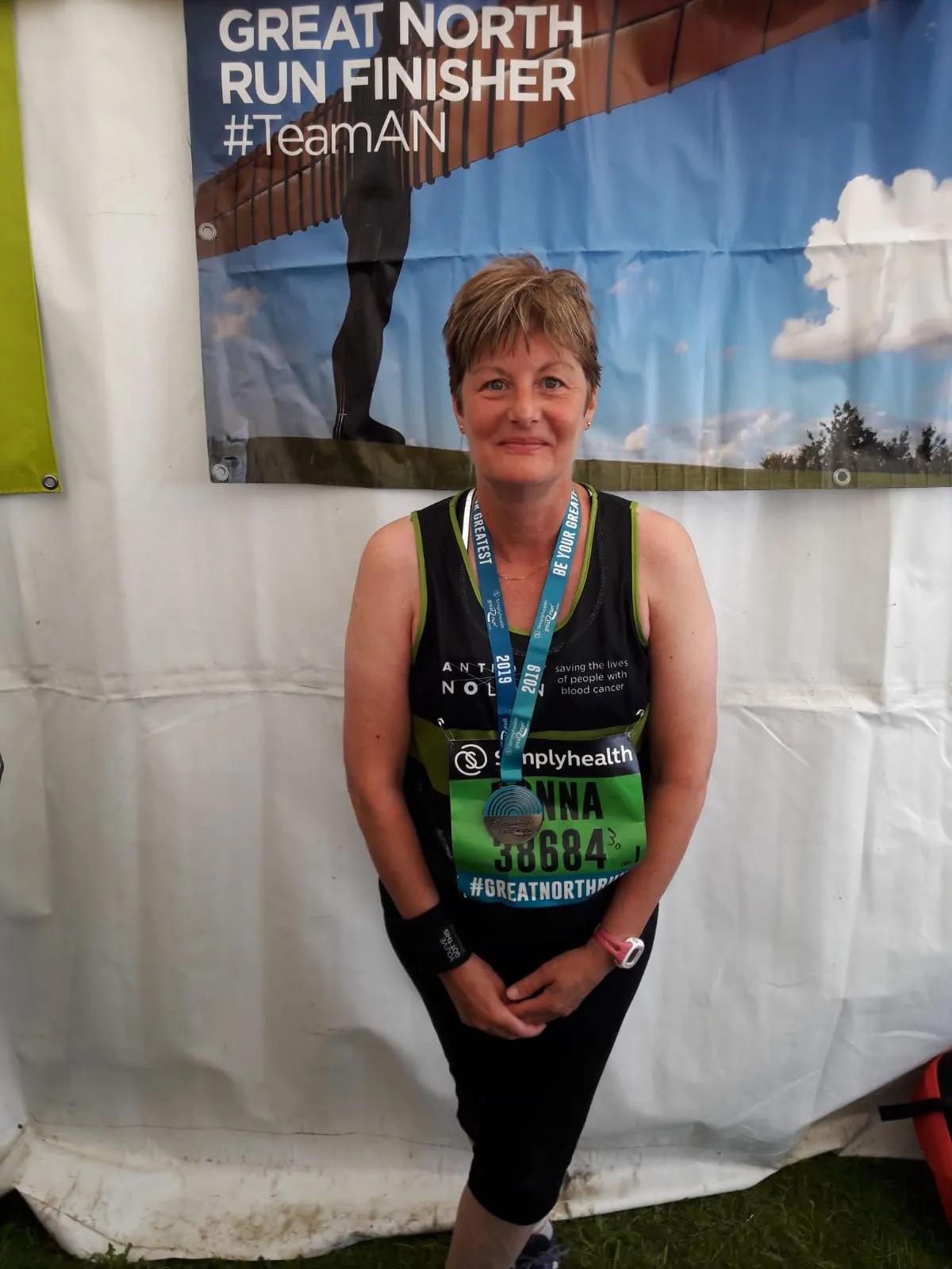 A woman wearing an Anthony Nolan running vest and medal around her neck