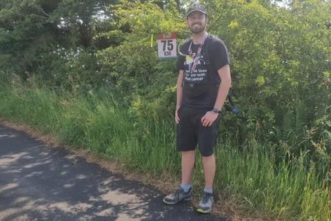 Photo of man in Anthony Nolan shirt smiling at a 75km marker 