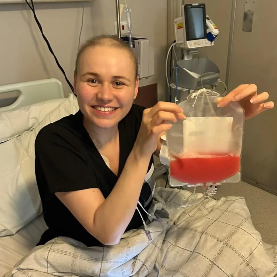 Faith smiling sat in hospital bed holding  bag of stem cells on the right of photo