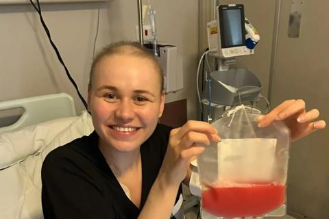 Faith smiling sat in hospital bed holding  bag of stem cells on the right of photo