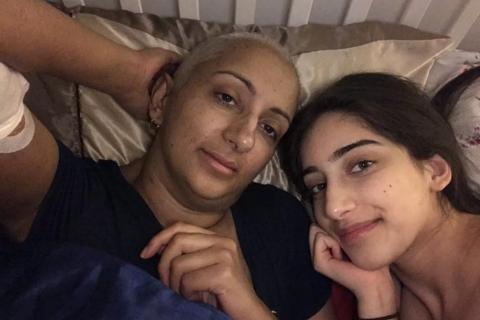 Kal, a South Asian woman with shaved hair, with her teenage daughter, both are lying on a bed smiling