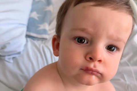 A baby boy is sat up in a hospital bed