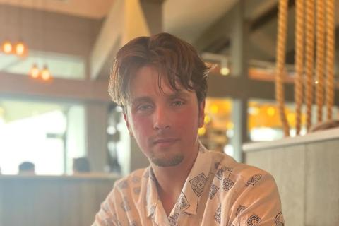 Photo of a young man sat at a restaurant table looking at the camera