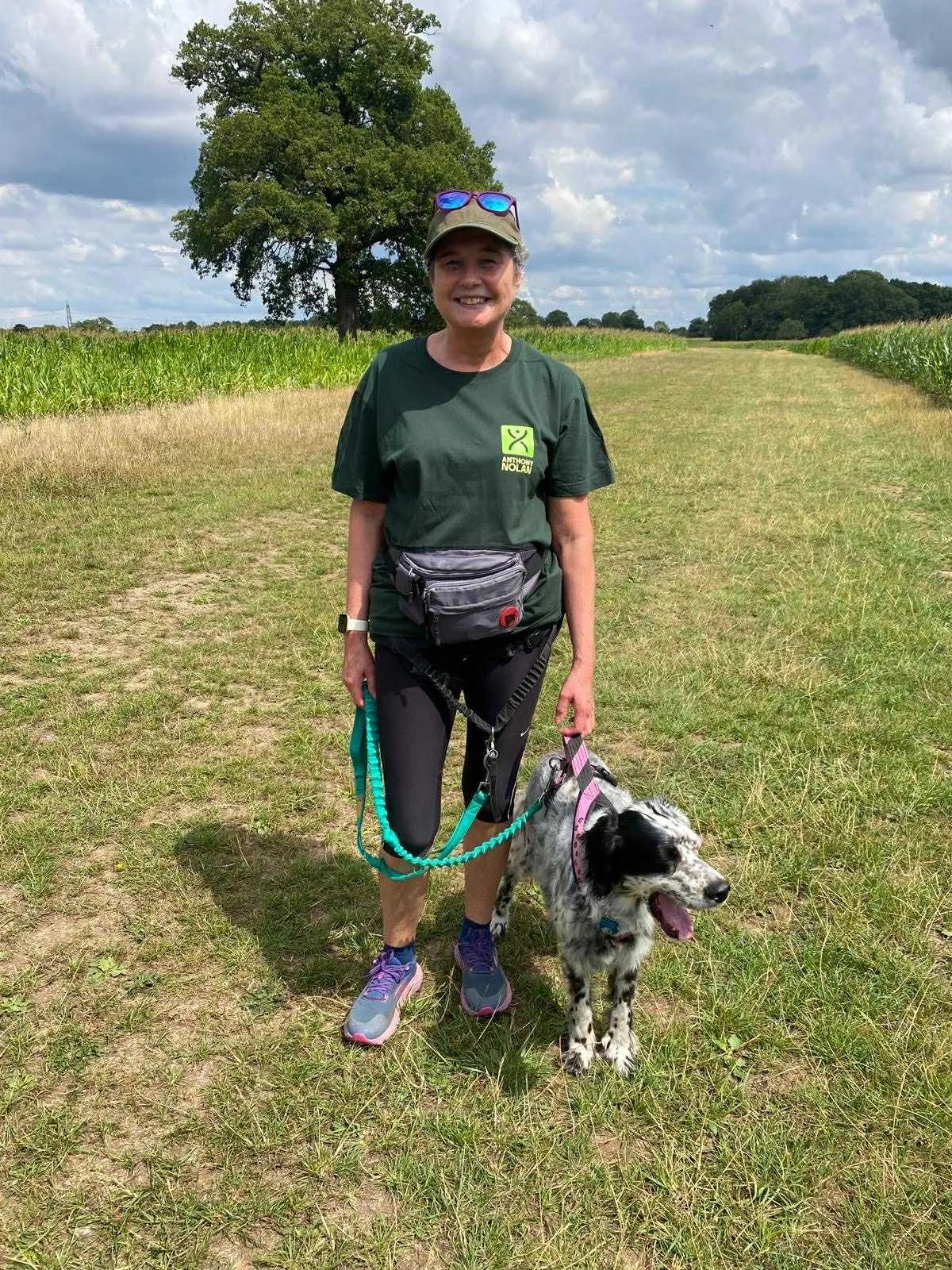 a woman in  a field with her dog, she's wearing an Anthony Nolan t-shirt and a cap