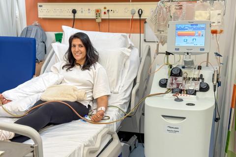 A female member of staff lying in a hospital bed donating stem cells smiling at the camera