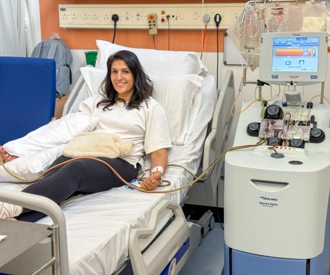 A female member of staff lying in a hospital bed donating stem cells smiling at the camera