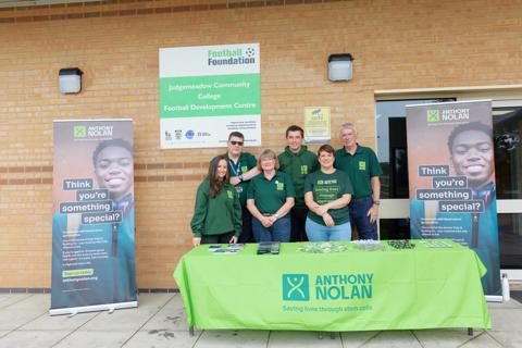 A team of volunteers standing behind a table set up with Anthony Nolan branded promotional material