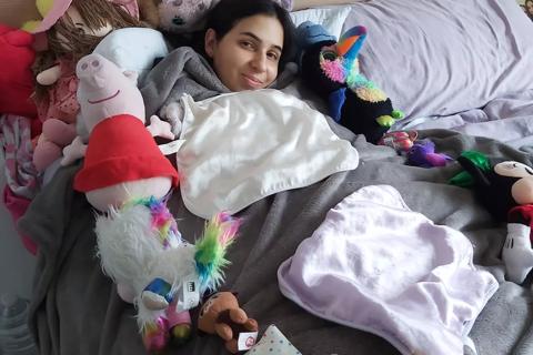 A woman with dark hair in bed surrounded by cuddly toys