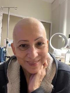 a selfie style photo of joanna who  has a bald head and is smiling, she's wearing a dark hoody with fleece lining
