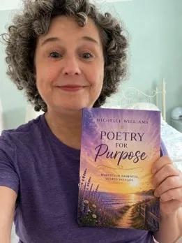 Michelle in a purple tshirt holding up a copy of her book