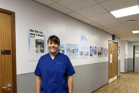 Emily in her blue nurse scrubs smiling for the camera in a hospital corridor