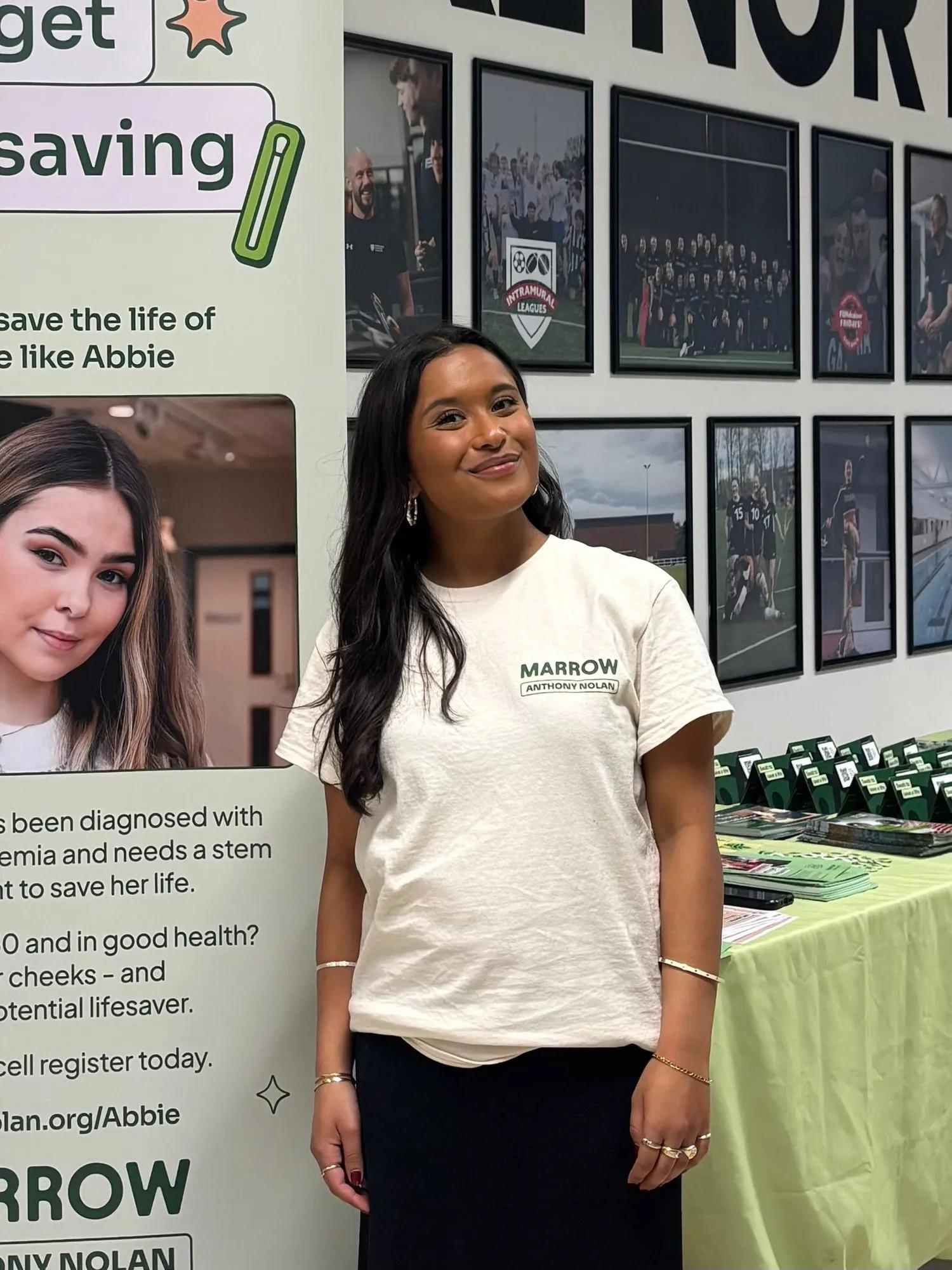 A young woman in a Marrow t-shirt standing in front of a donor recruitment stall