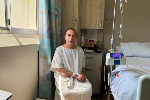 A middle aged man wearing a hospital gown sits in a hospital room