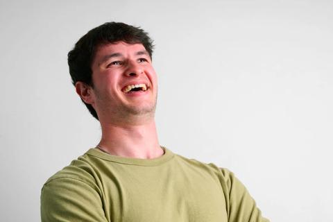 A 22 year old white male in a beige tshirt laughing looking away from the camera with his head back