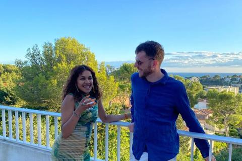 Theo and his fiancee Rebekah stood on a balcony in the sunshine, with a view of greenery and blue skies behind them