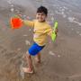 Picture of five-year-old Eesa Hussain on the beach. Eesa is holding a red bucket and green spade as he stands on the shore. 